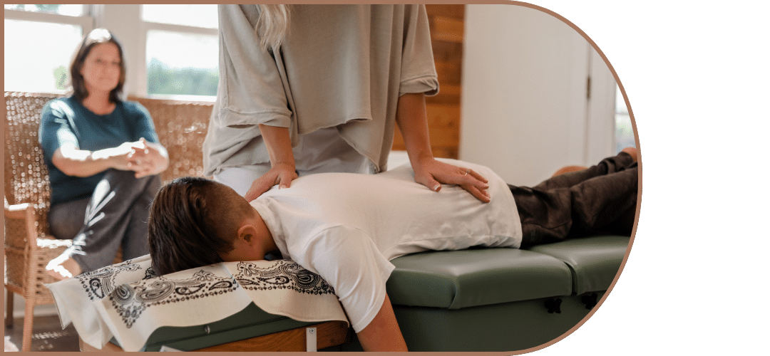 Child receiving chiropractic treatment on a therapy table, with a chiropractor gently applying pressure, while a parent observes in the background, emphasizing pediatric care at The Chiro Co.